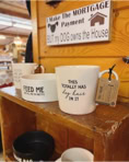 Shelves displaying mugs with humorous text and a sign above about a dog owning the house.