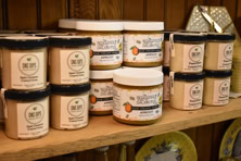 Jars of honey and spreads on a wooden shelf with decorative plates in the background.