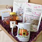 Gift box containing a mug with a pumpkin and sunflower design, a jar of honey, a package of English tea scone mix, a bag of loose leaf tea blend, and a small card, all nestled in purple shredded paper.